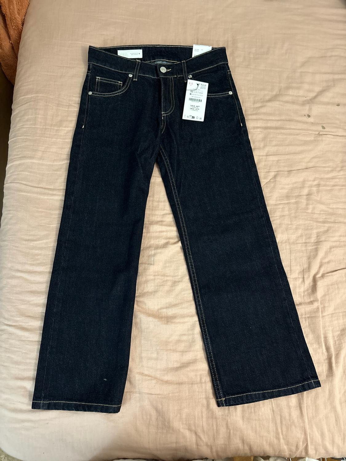 Dark blue jeans with contrasting stitching and labels, spread out on a beige sheet.
