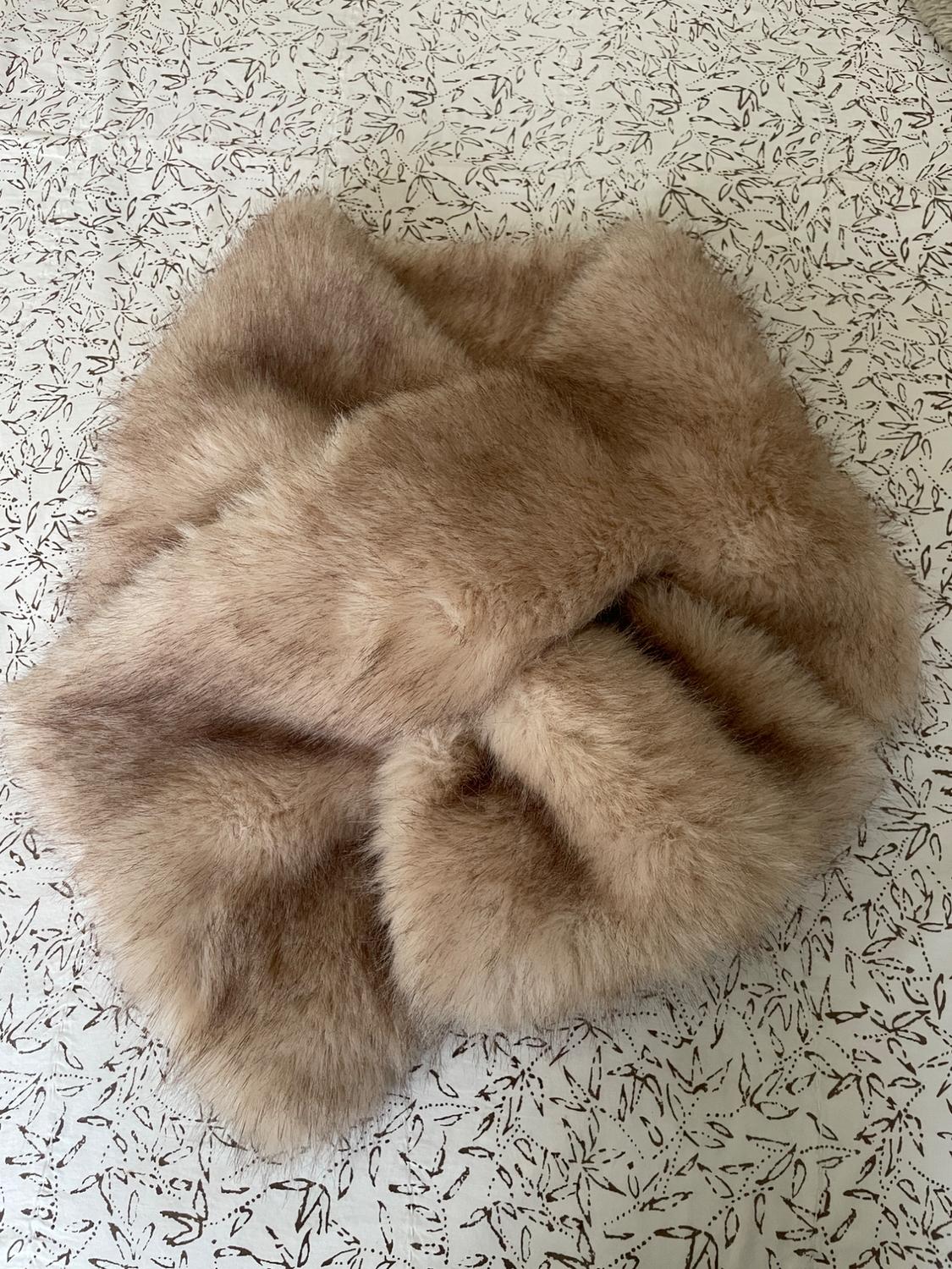 Beige faux fur scarf on a surface with a black and white leaf pattern.