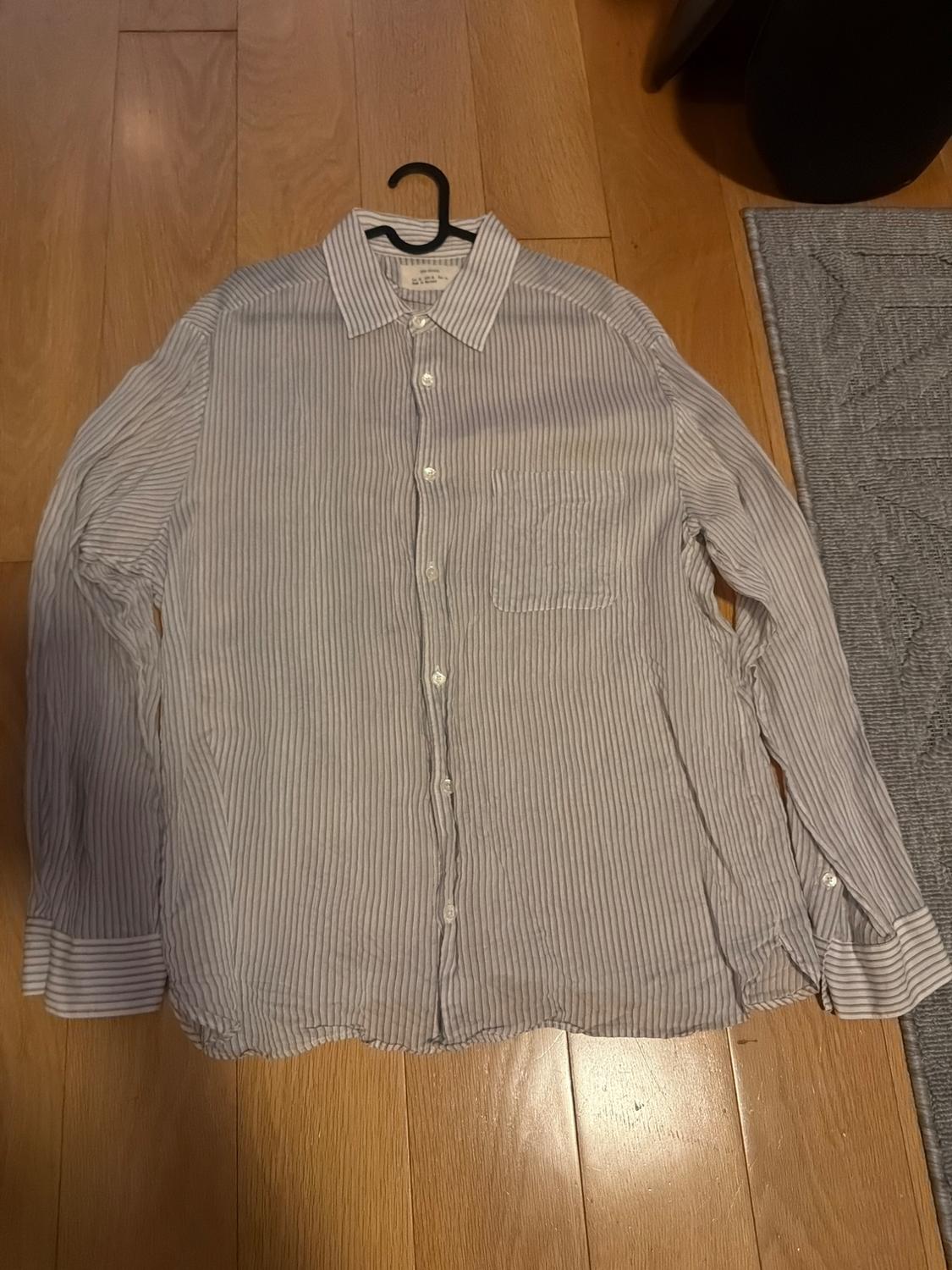 White and gray striped shirt hanging on a black hanger over a light wood floor.