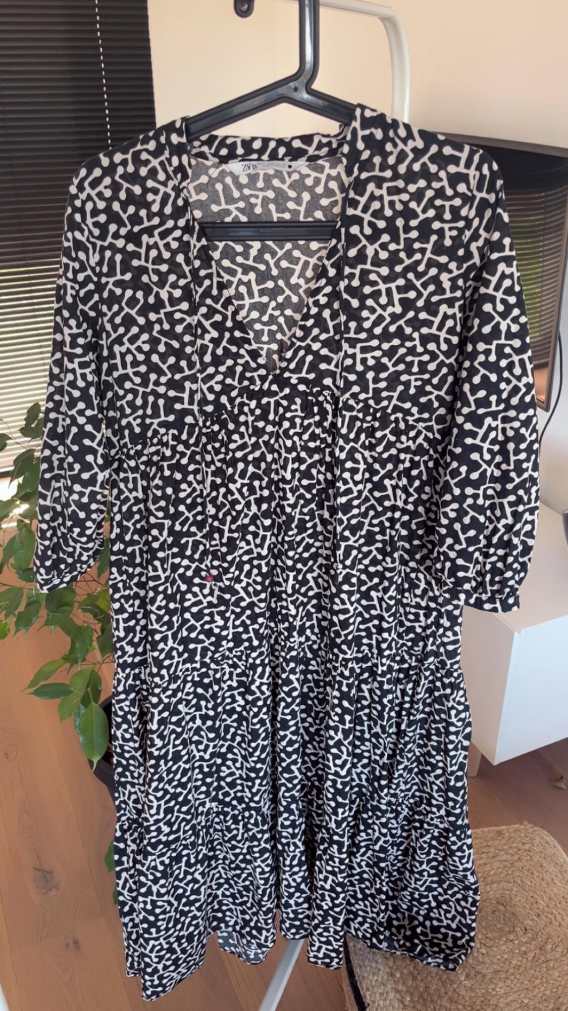 Dress hanging on a hanger with a black and white abstract pattern. Interior background with a plant and furniture.