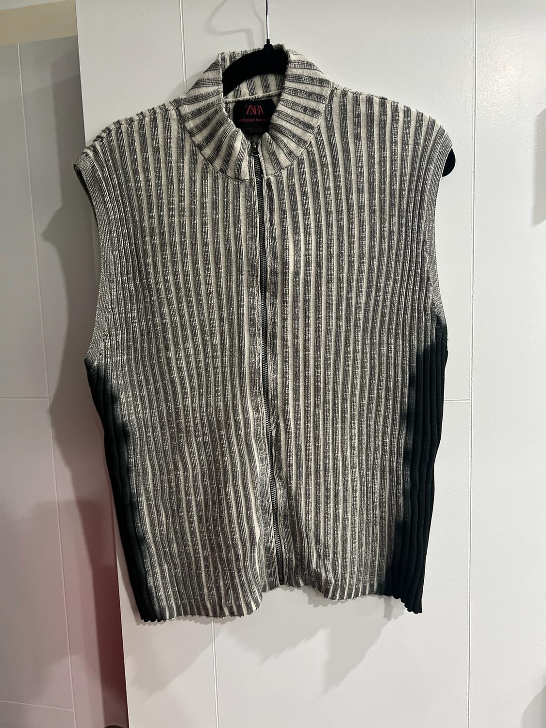 Striped knit waistcoat with zip, high neck and black sides, hanging on a hanger against a white background. ZARA label.
