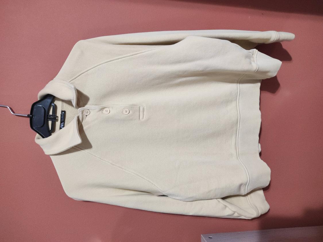 Beige jumper with collar and buttons hanging on a black hanger against a pink wall.