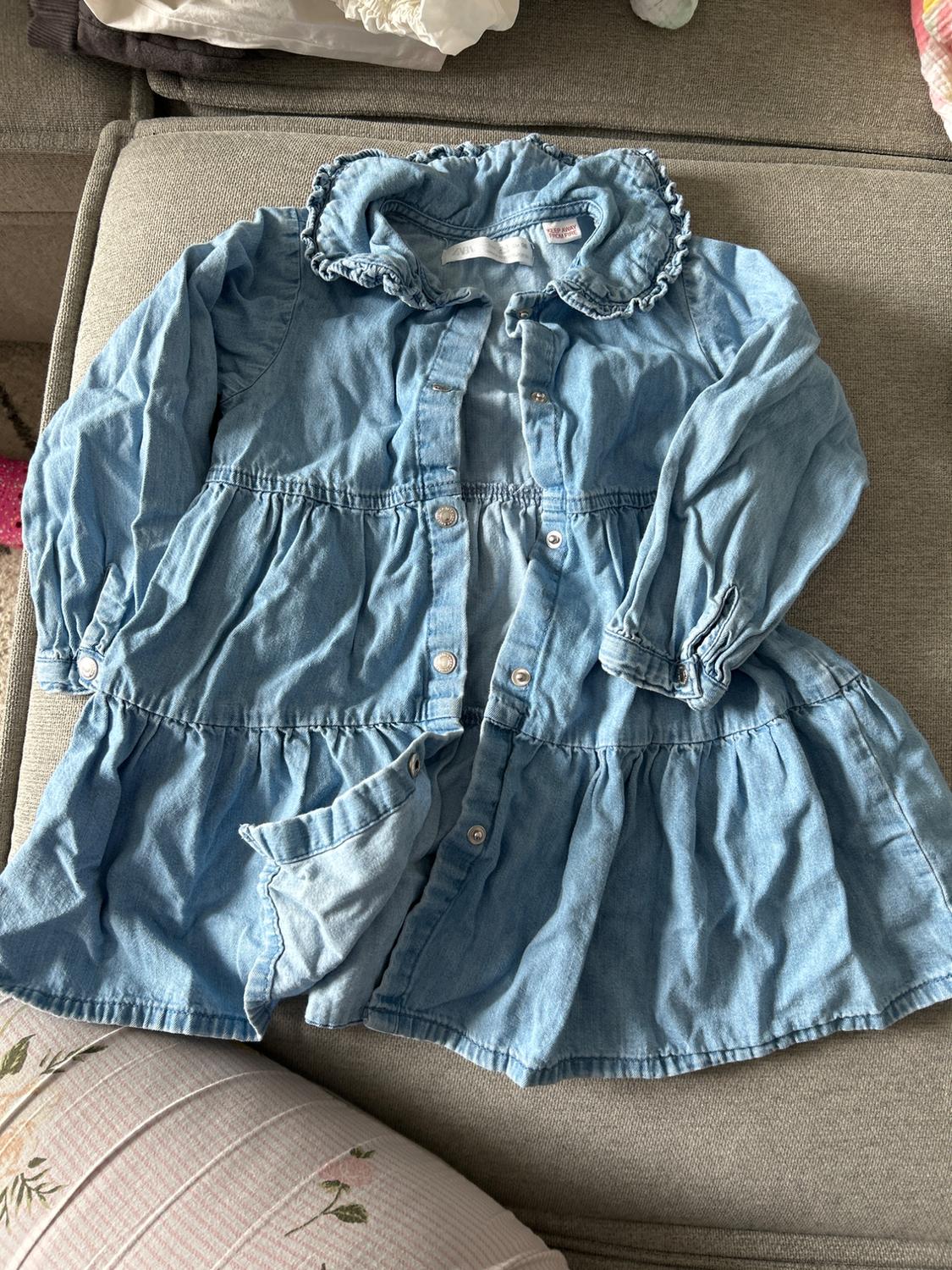 Light blue denim dress with a ruffled collar and buttons, on a grey sofa. Part of a floral cushion visible.
