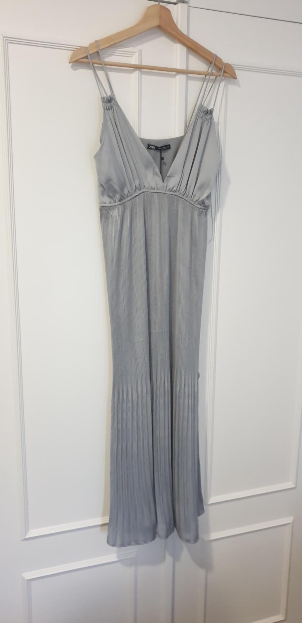 Grey maxi dress with spaghetti straps and a V-neckline, hanging on a wooden hanger over a white door.