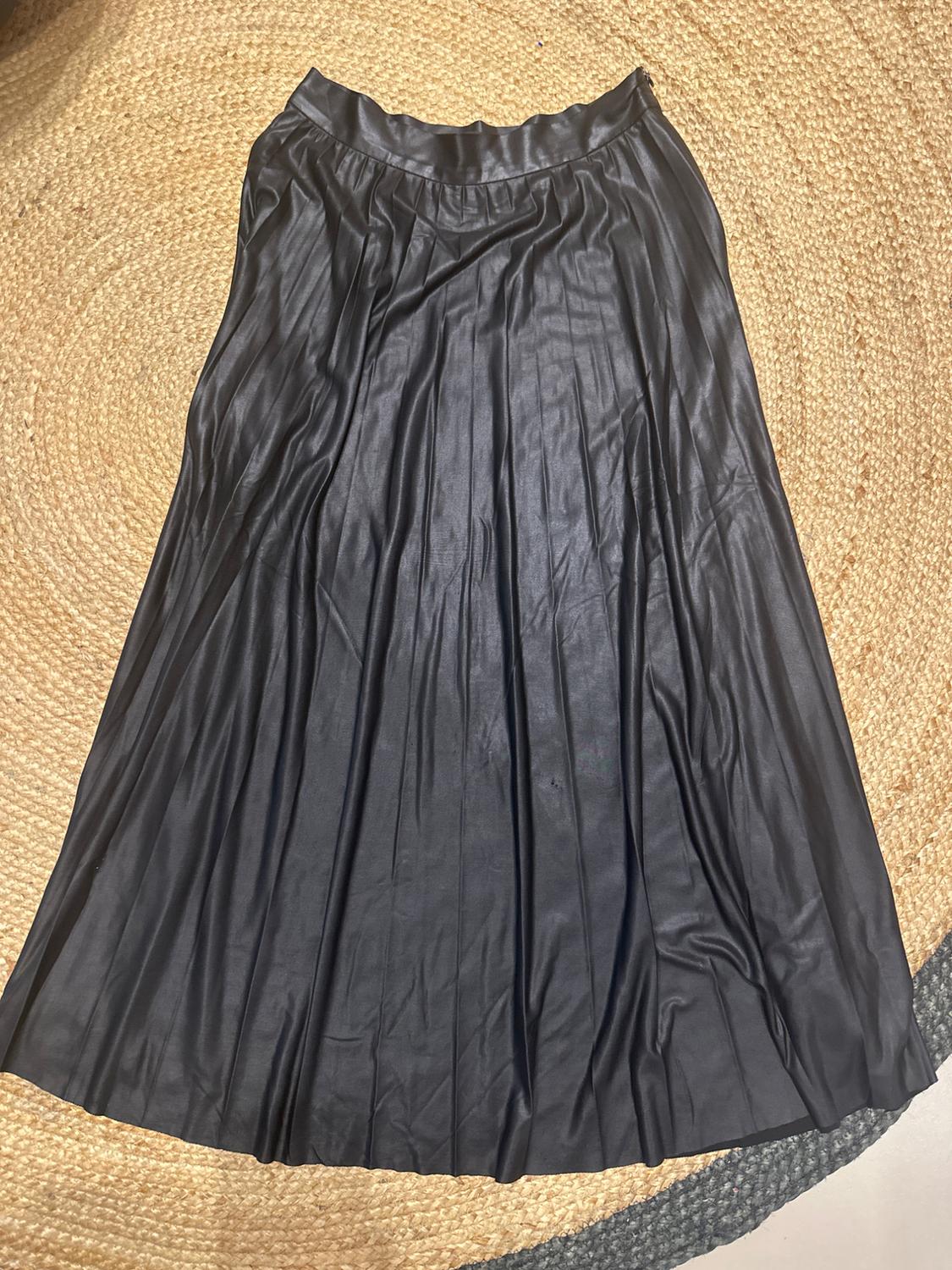 Black pleated skirt made of shiny material on a braided jute rug.