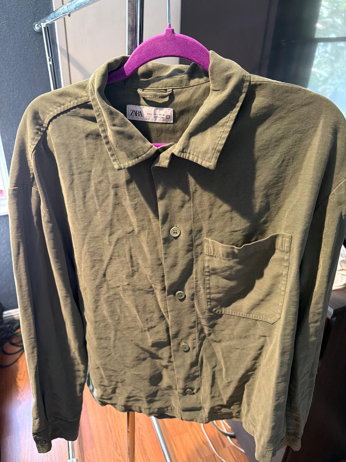 Olive green button-down shirt with a pocket on a purple hanger. Label with text: ZARA EUR L USA L MEX 42 MADE IN CHINA.