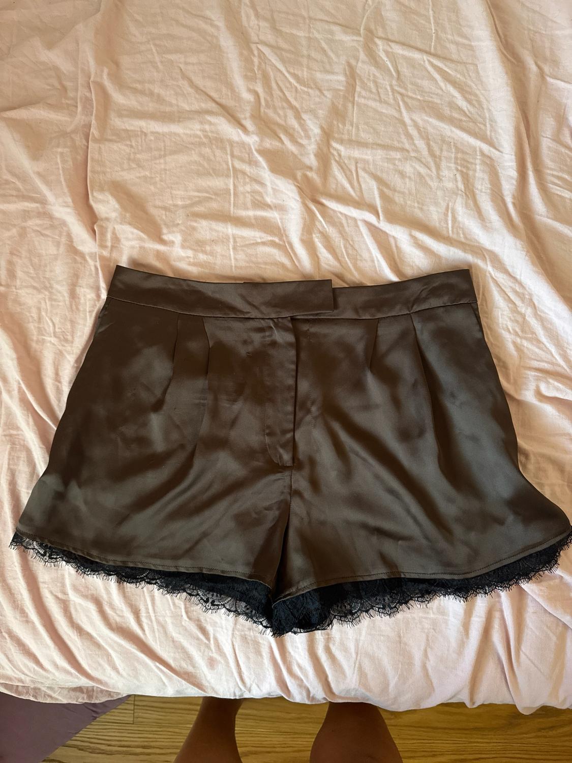 Brown satin shorts with black lace trim at the hem, on a pink sheet. Legs are visible at the bottom.