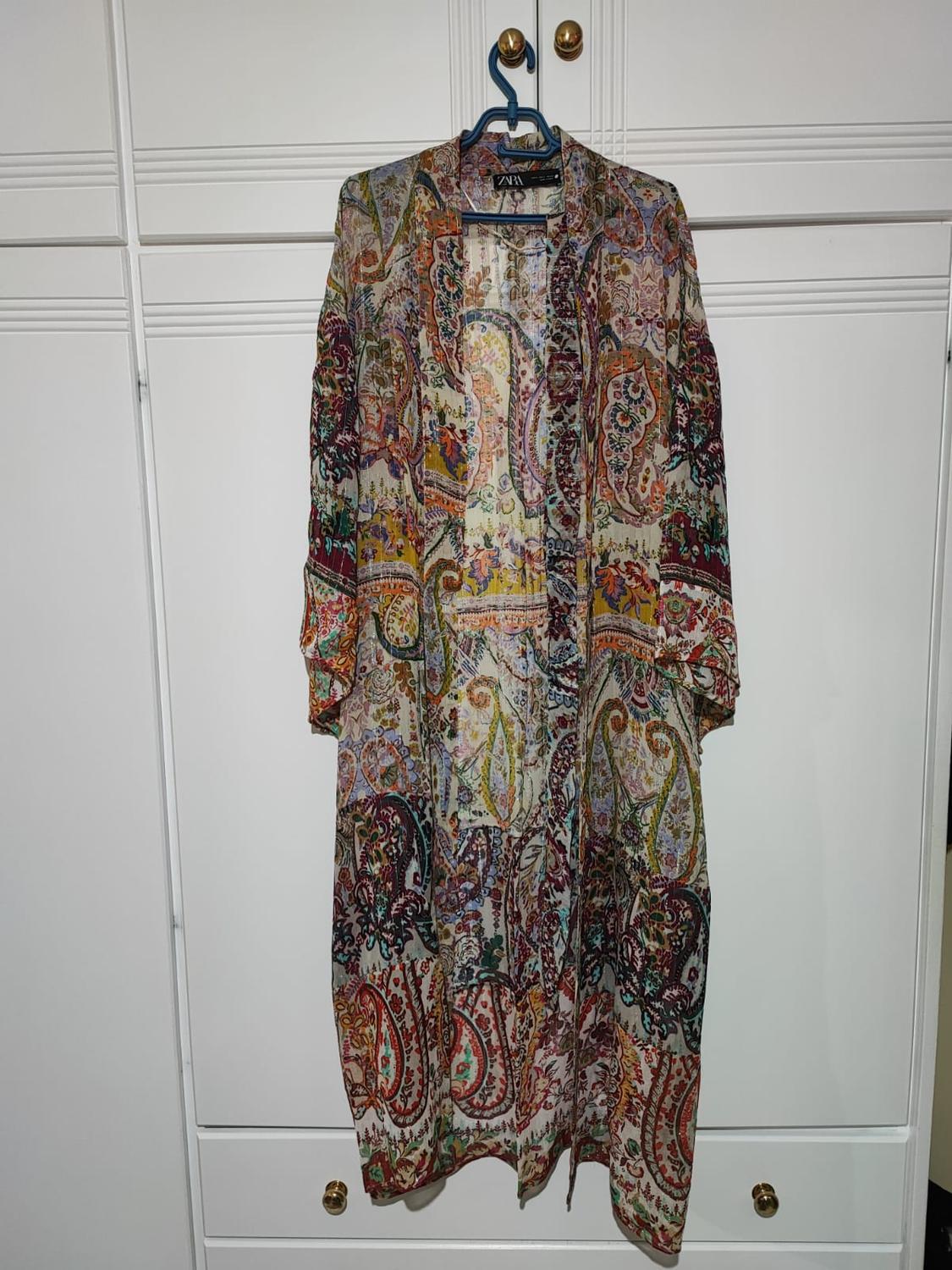 Long dress with colourful print hanging on a blue hanger in front of a white wardrobe with gold handles.