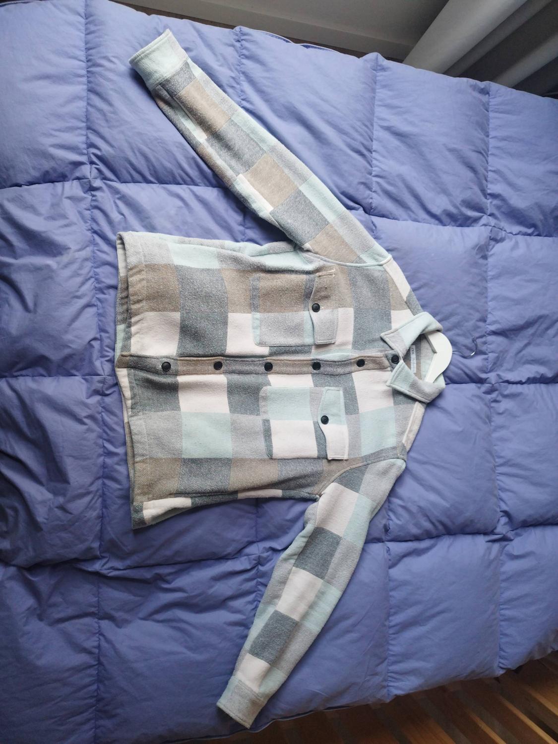 Checkered shirt in pastel shades on a blue quilt. The shirt has dark buttons and a chest pocket.