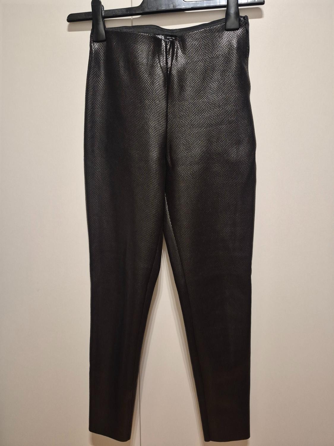 Black trousers hanging on a hanger, with a geometric pattern texture, against a light background.