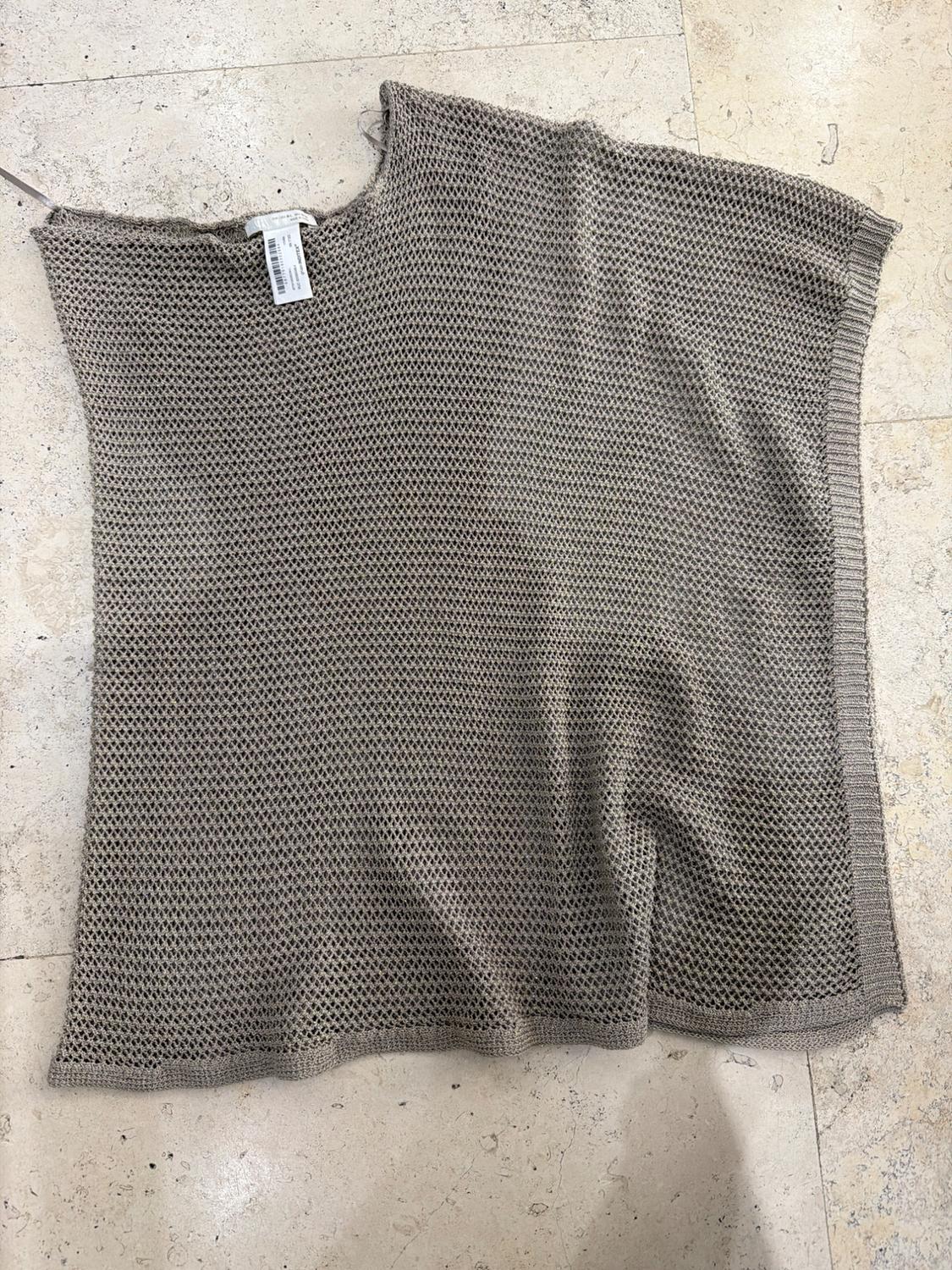Beige open-knit top laid out on a light-tiled floor. Relaxed style with a visible label at the neck.