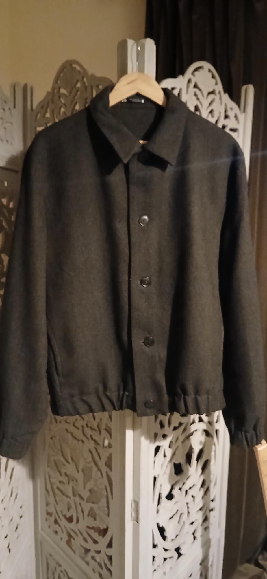 A dark grey jacket with black buttons is hanging on a wooden coat rack, with a carved white room divider in the background.