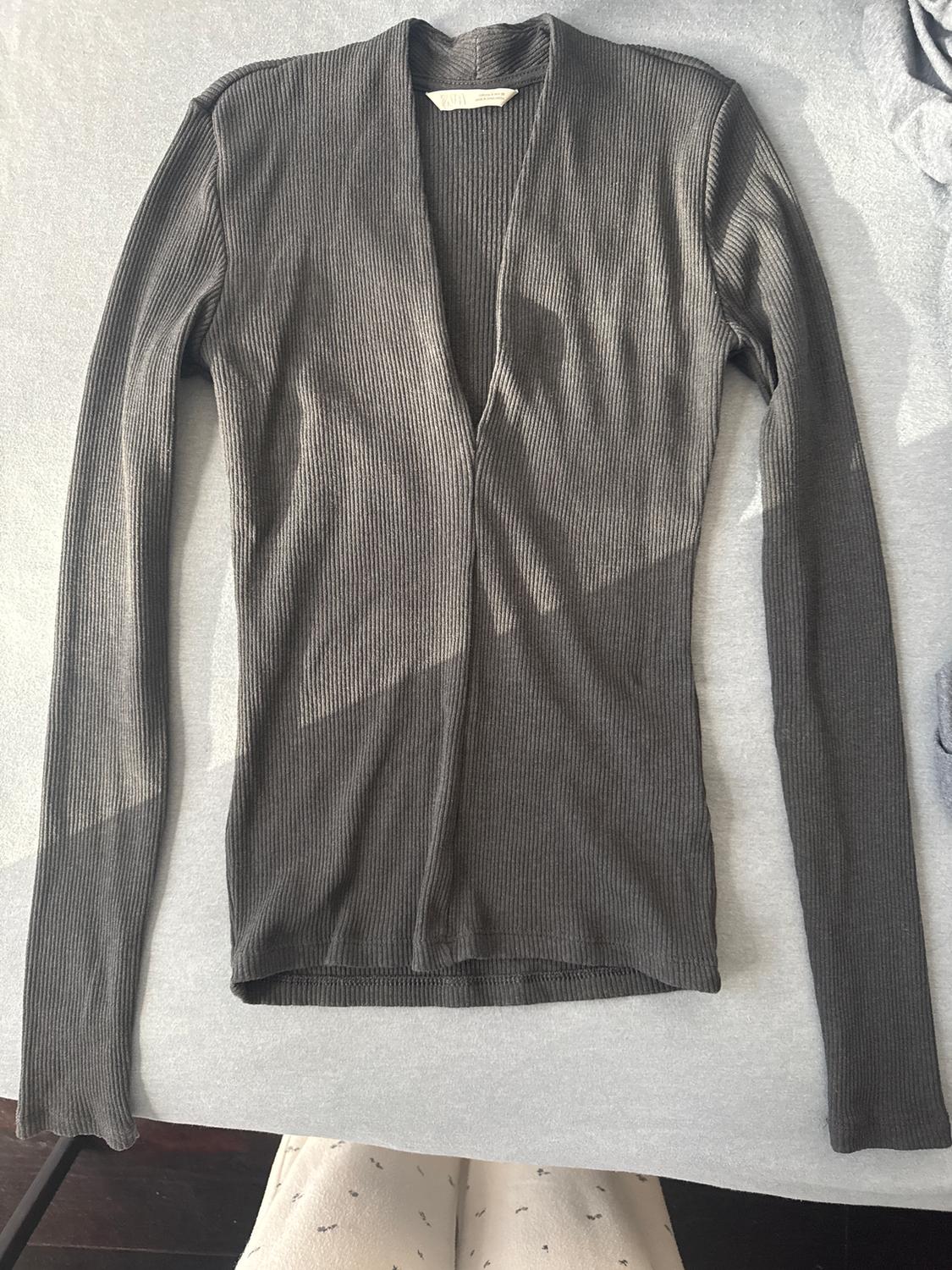 Grey, long-sleeved, ribbed cardigan on a light surface. Visible neck label.