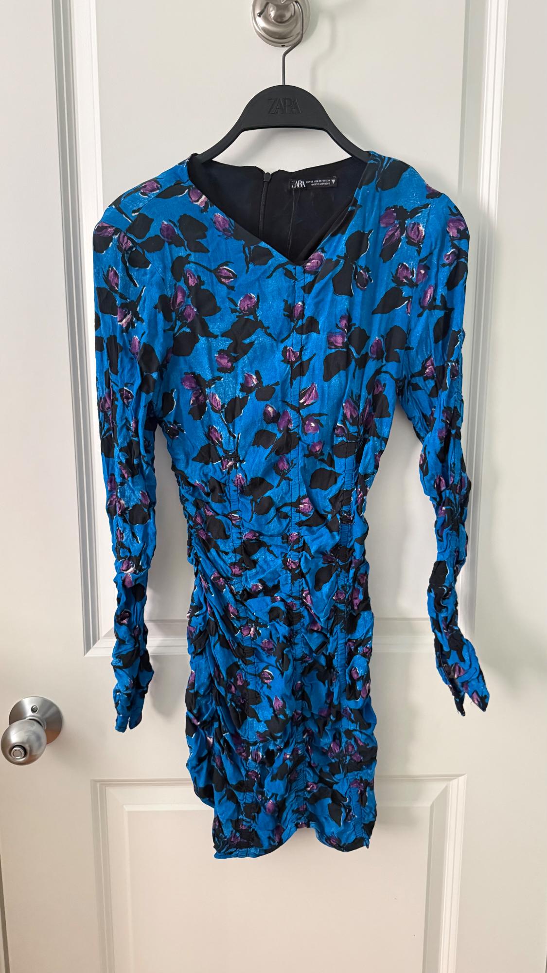 Blue dress with black and purple floral print, hanging on a black Zara hanger over a white door.
