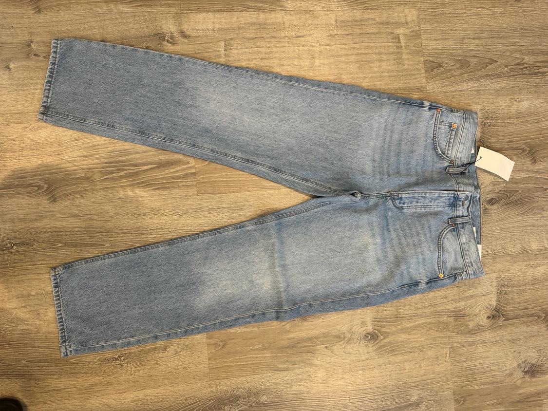 Light blue jeans laid out on a wooden floor, with a white label on the waistband.