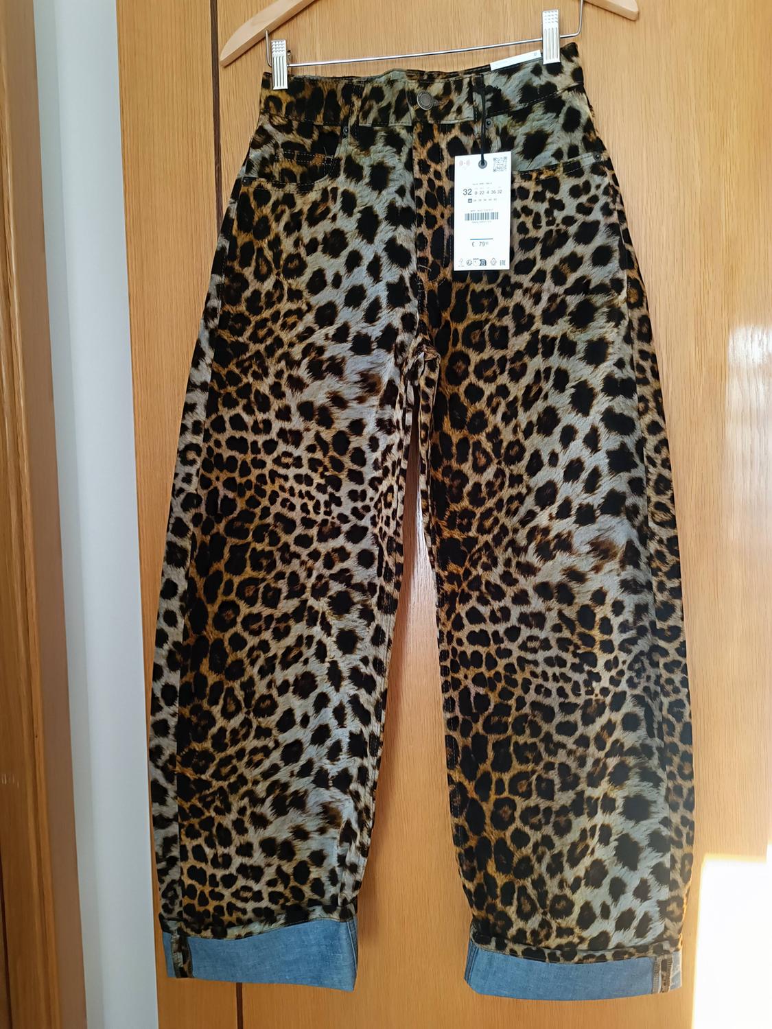 Leopard print trousers hanging on a wooden hanger, with a visible tag in the top right corner.