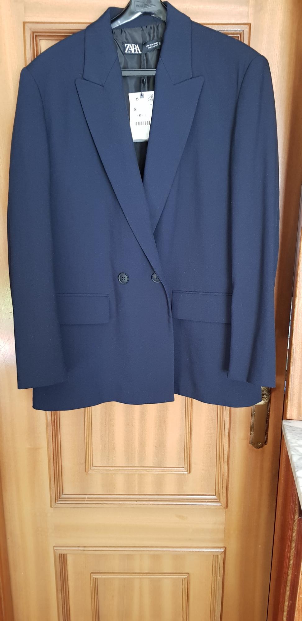 Navy double-breasted jacket hanging on a wooden door. Visible label with brand and size S.