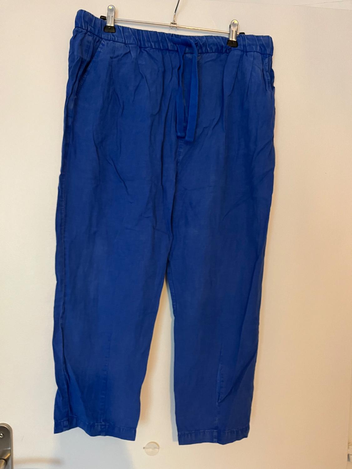 Casual blue trousers with an elasticated waistband and drawstring, hanging from a metal hanger on a white door.