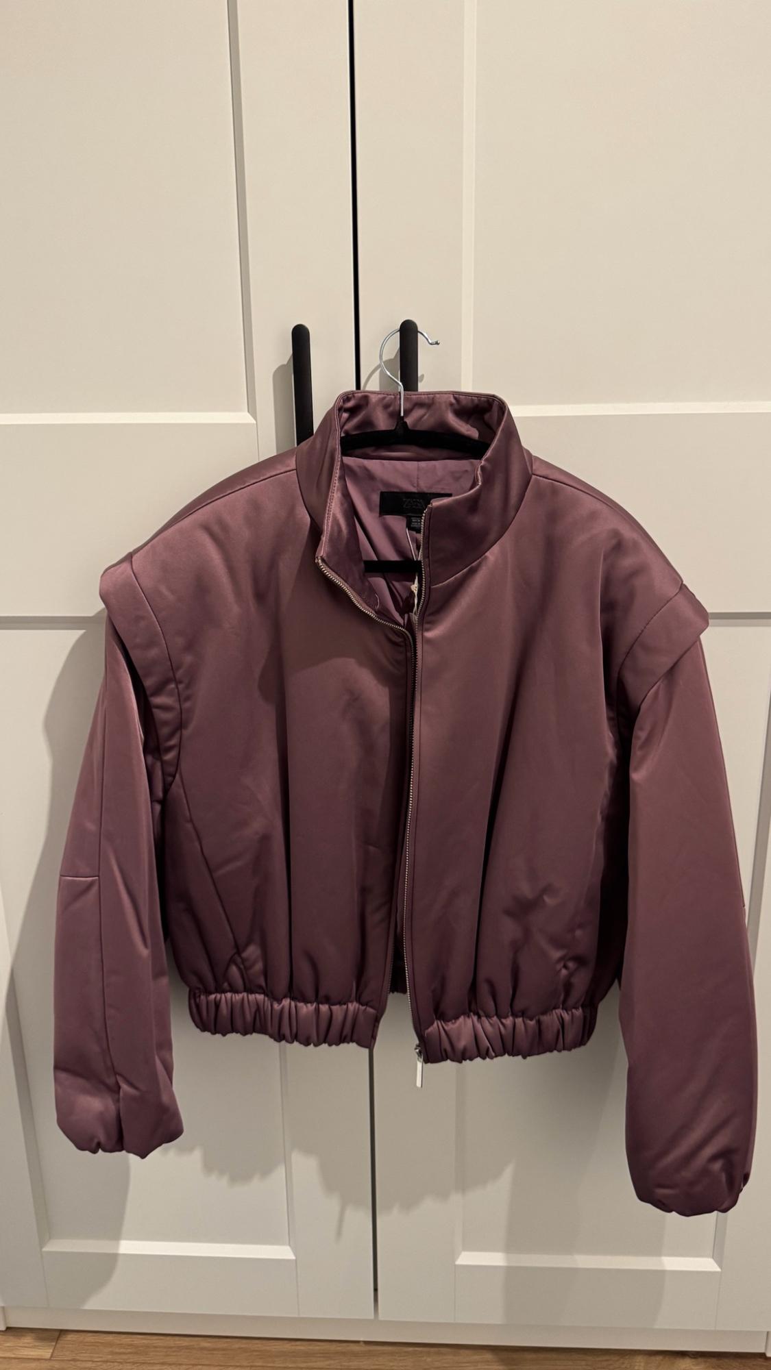 Mauve padded jacket with zip, hanging on a hanger over a white wardrobe with black handles. Label with text ZARA.