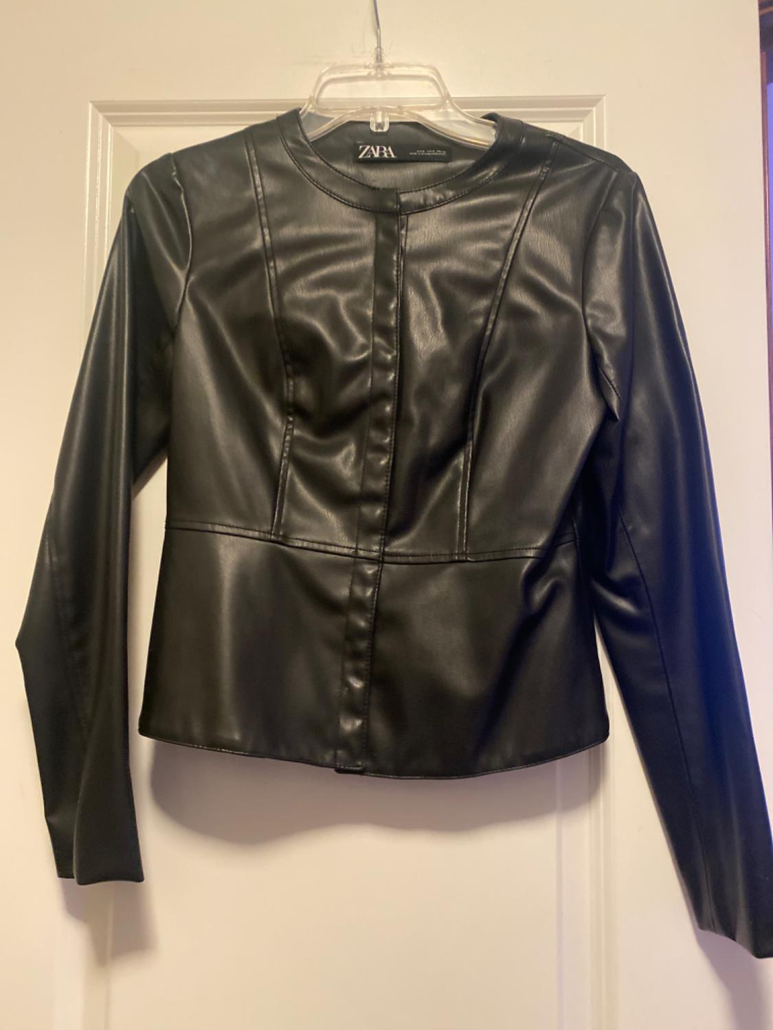 Black synthetic jacket hanging on a clear hanger over a white door. Visible label: ZARA.