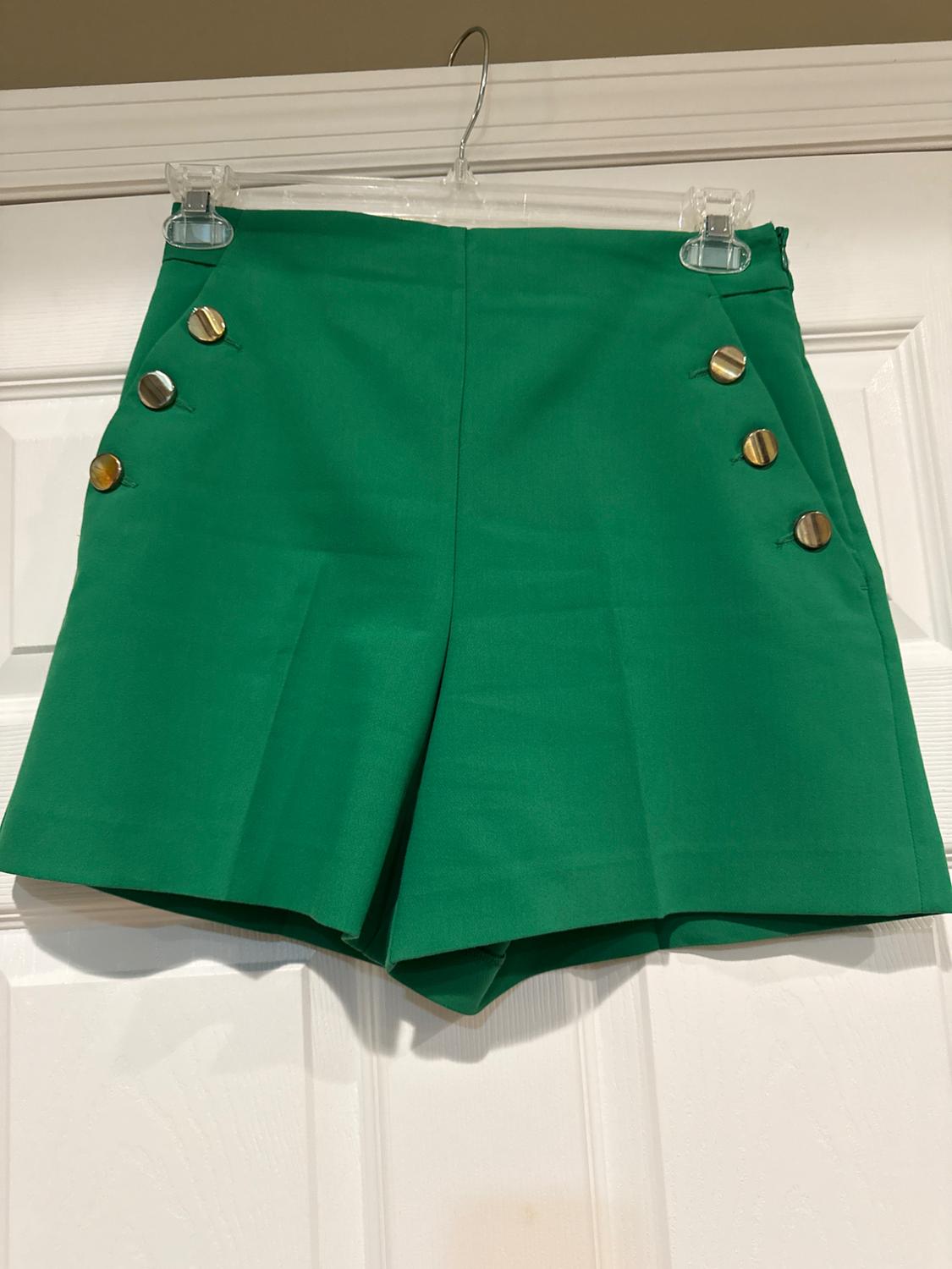 Front view of green shorts with gold buttons on the sides.