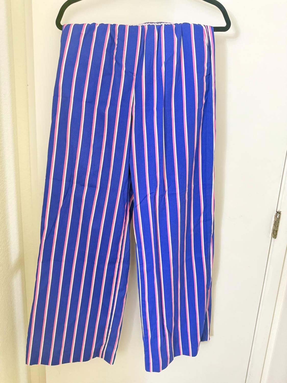 Trousers hanging with a vertical striped print in blue, white and pink. White background and visible black hanger.