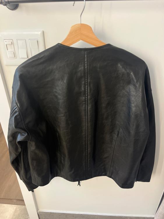 Black leather jacket hanging on a wooden hanger, viewed from behind, against a white background with visible switches.