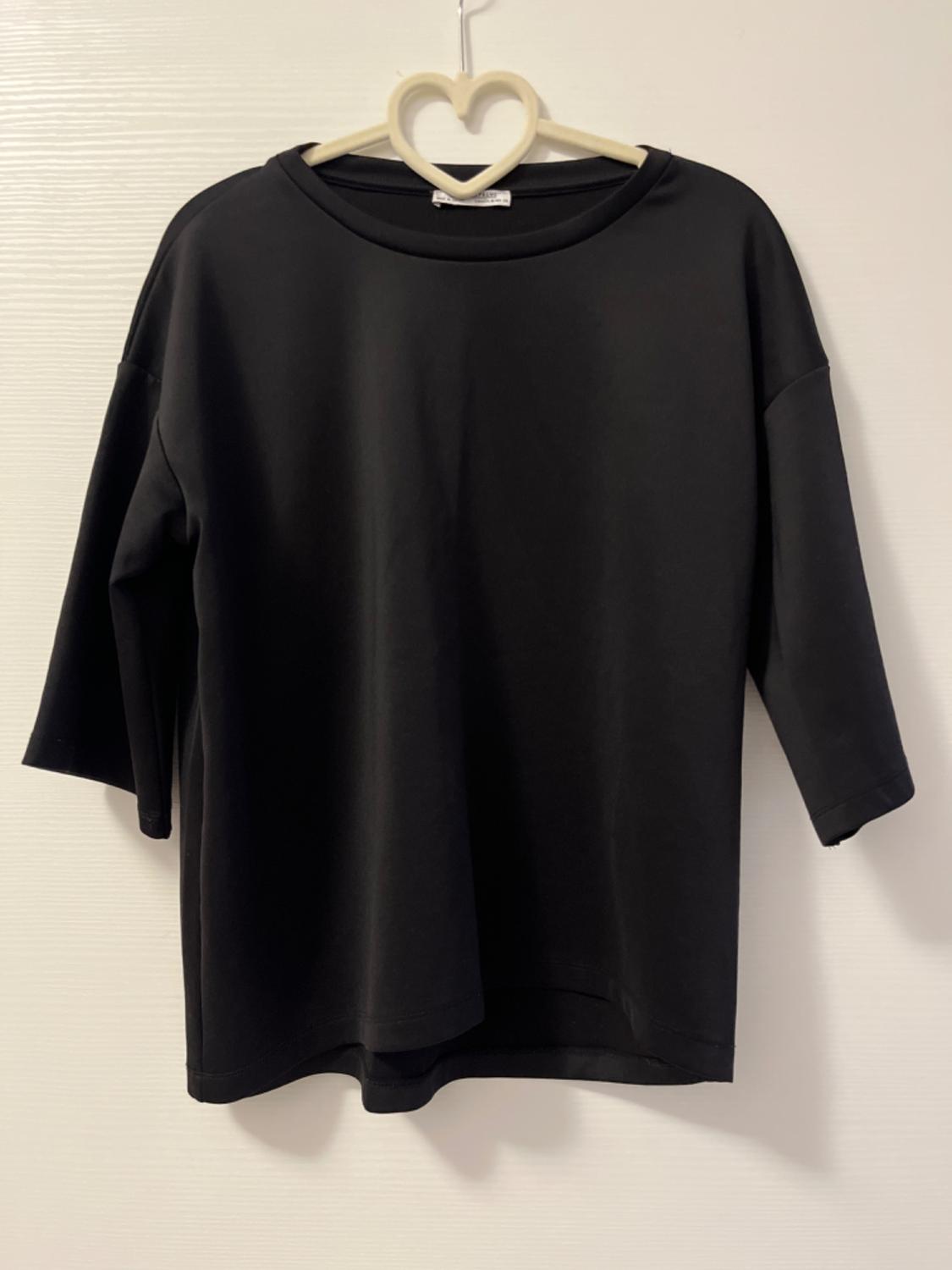 Plain black three-quarter-sleeve T-shirt hanging on a heart-shaped hanger against a white background.
