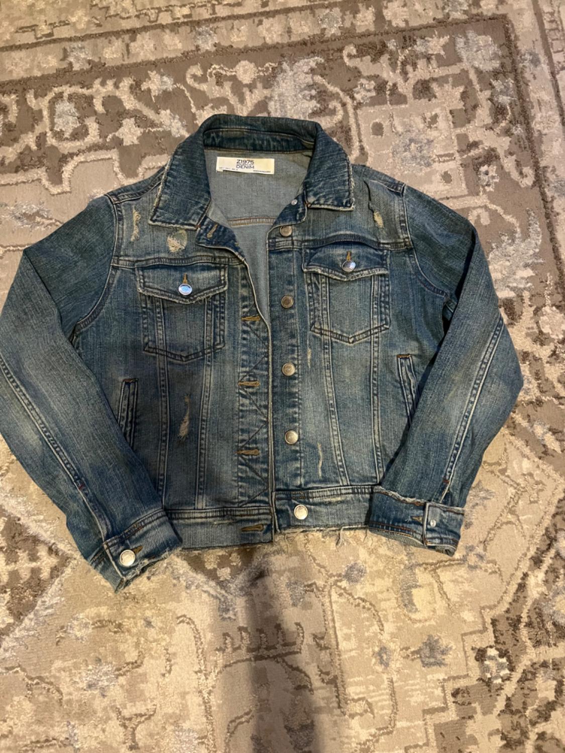 Worn blue denim jacket on a rug with a geometric design in beige and brown tones. Visible tag: "Z1975 DENIM".