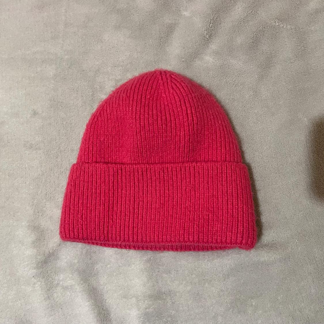 Red knitted hat on a grey surface. The knit is thick and has a simple design with a folded brim.