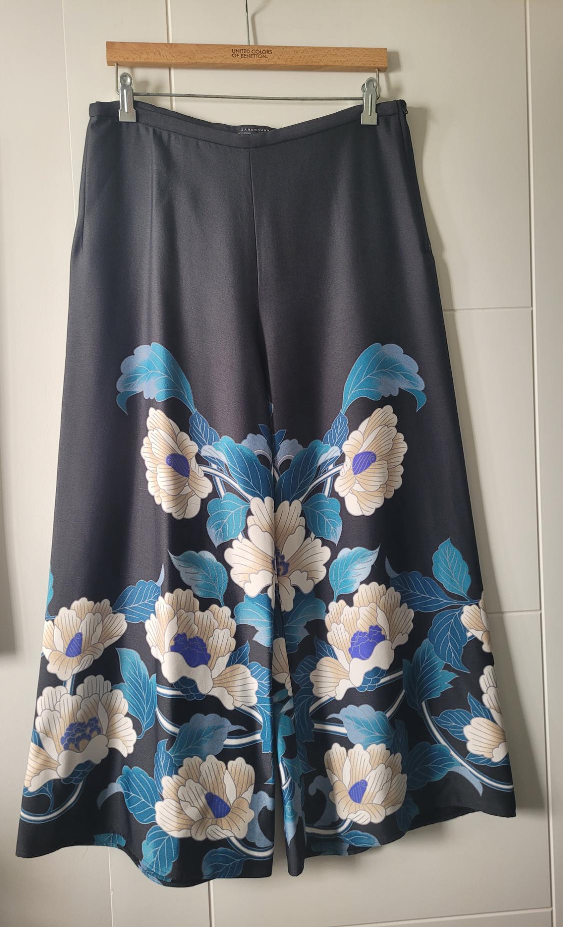 Black skirt with a floral print in shades of blue and beige, hanging on a wooden hanger with the text "United Colors of Benetton".