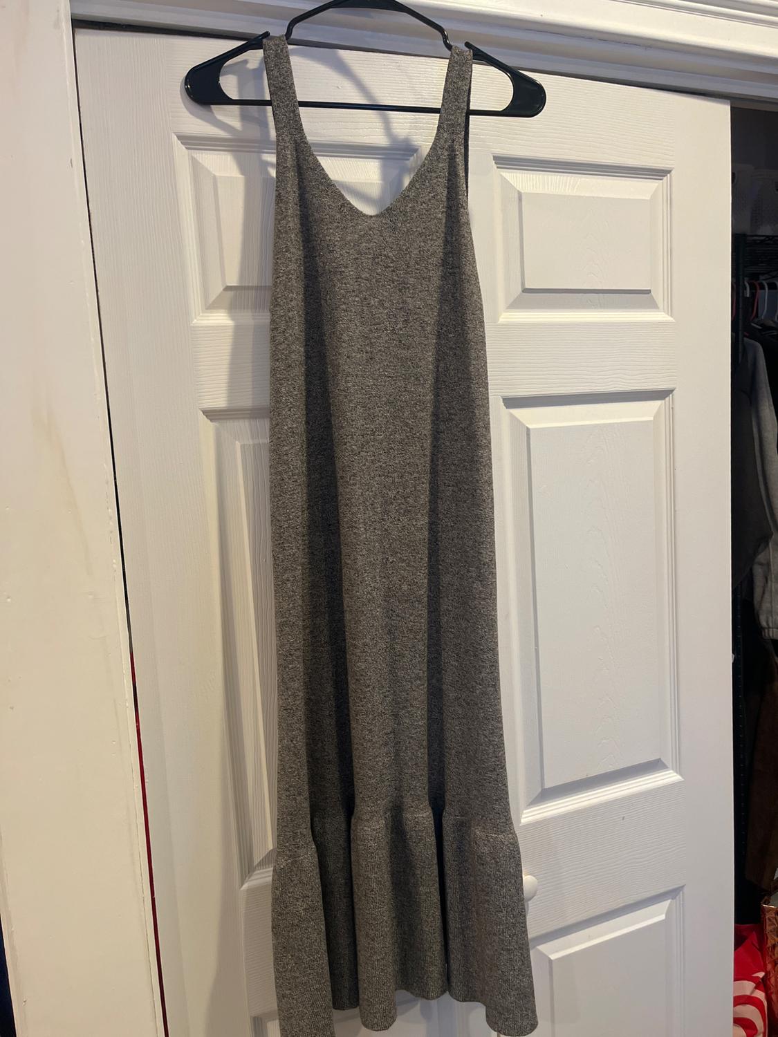 Sleeveless grey dress hanging on a black hanger in front of a white door. Simple design with a flared skirt.