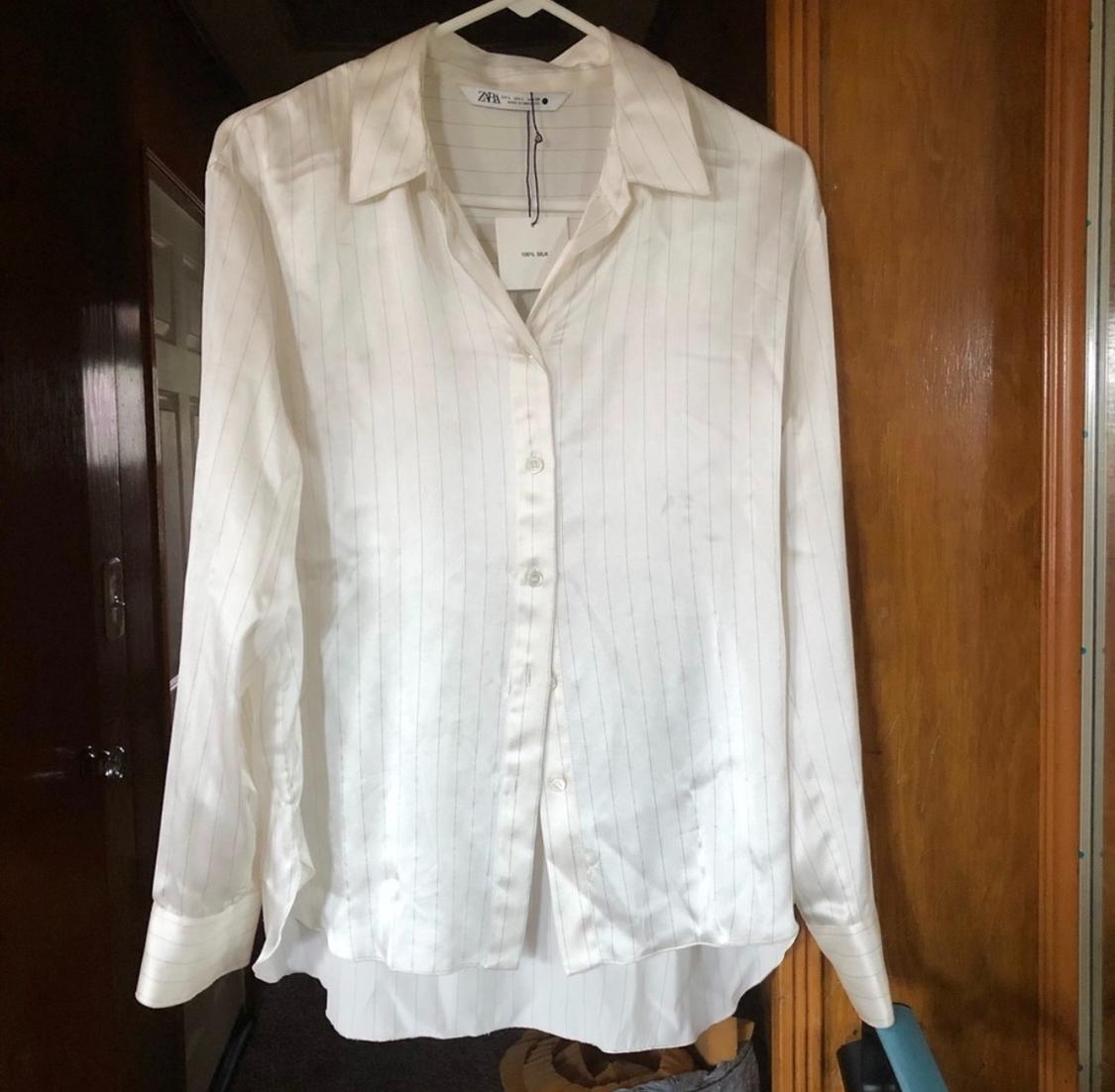 Fine-striped white shirt hanging on a hanger, with a wooden background and a dark door. Visible label on the collar.