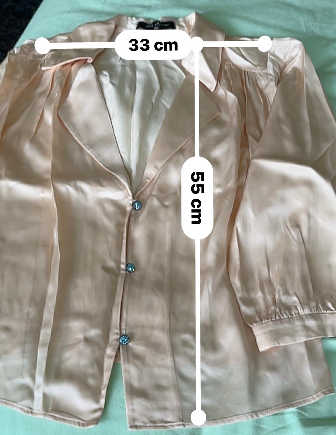 Peach-coloured satin blouse with blue buttons, measuring 33 cm wide and 55 cm long, on a green surface.