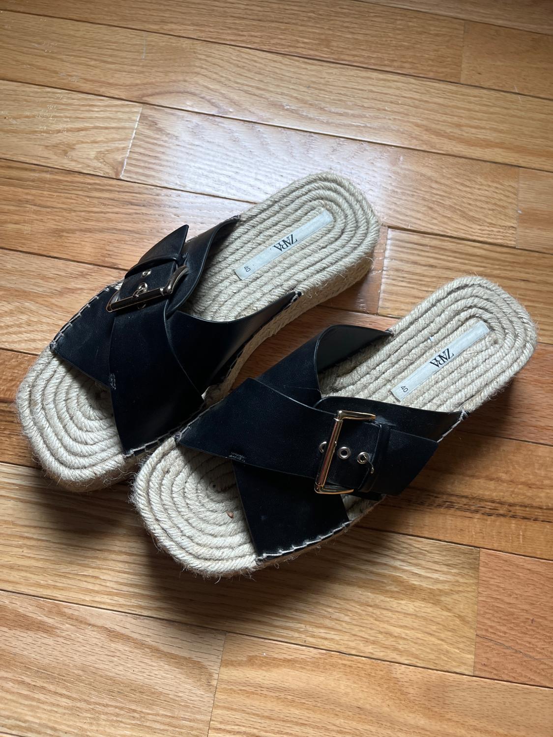 Black sandals with crossover straps, buckle and jute sole on a wooden floor. Casual style. Text: ZARA 40.