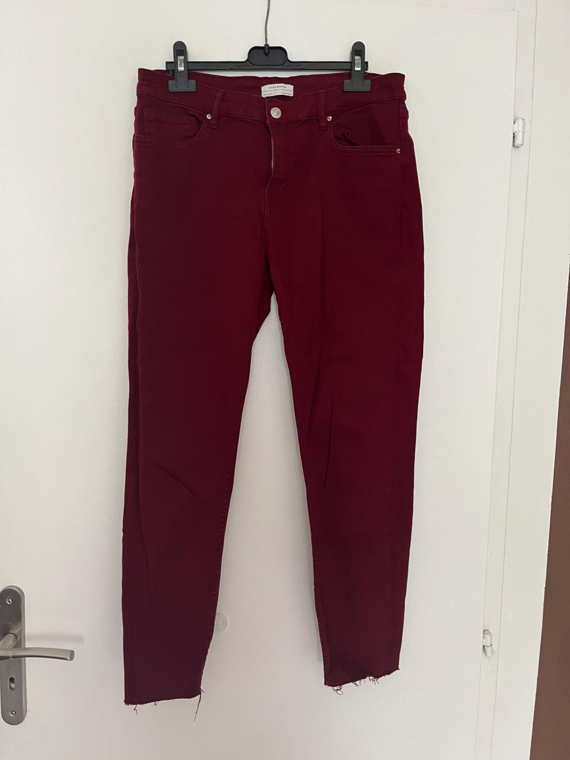 Front view of red trousers with front pockets and a frayed hem.