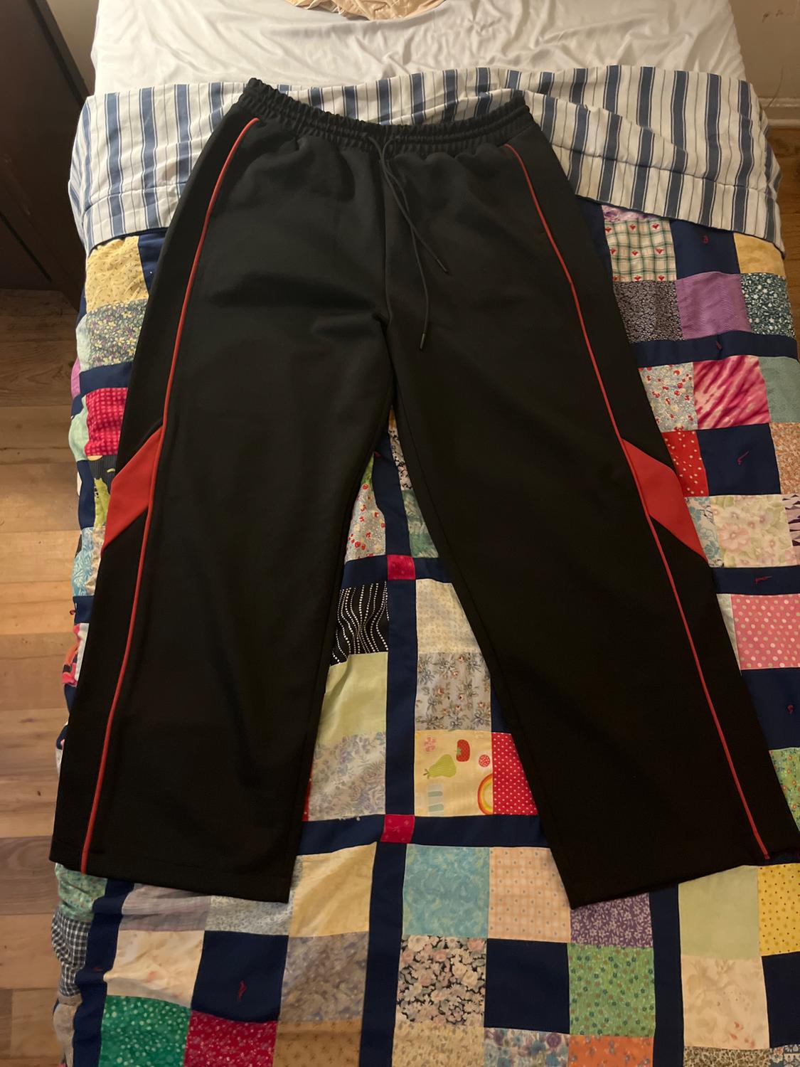 Black jogging bottoms with red stripes on a colourful patchwork quilt on a bed with striped sheets.