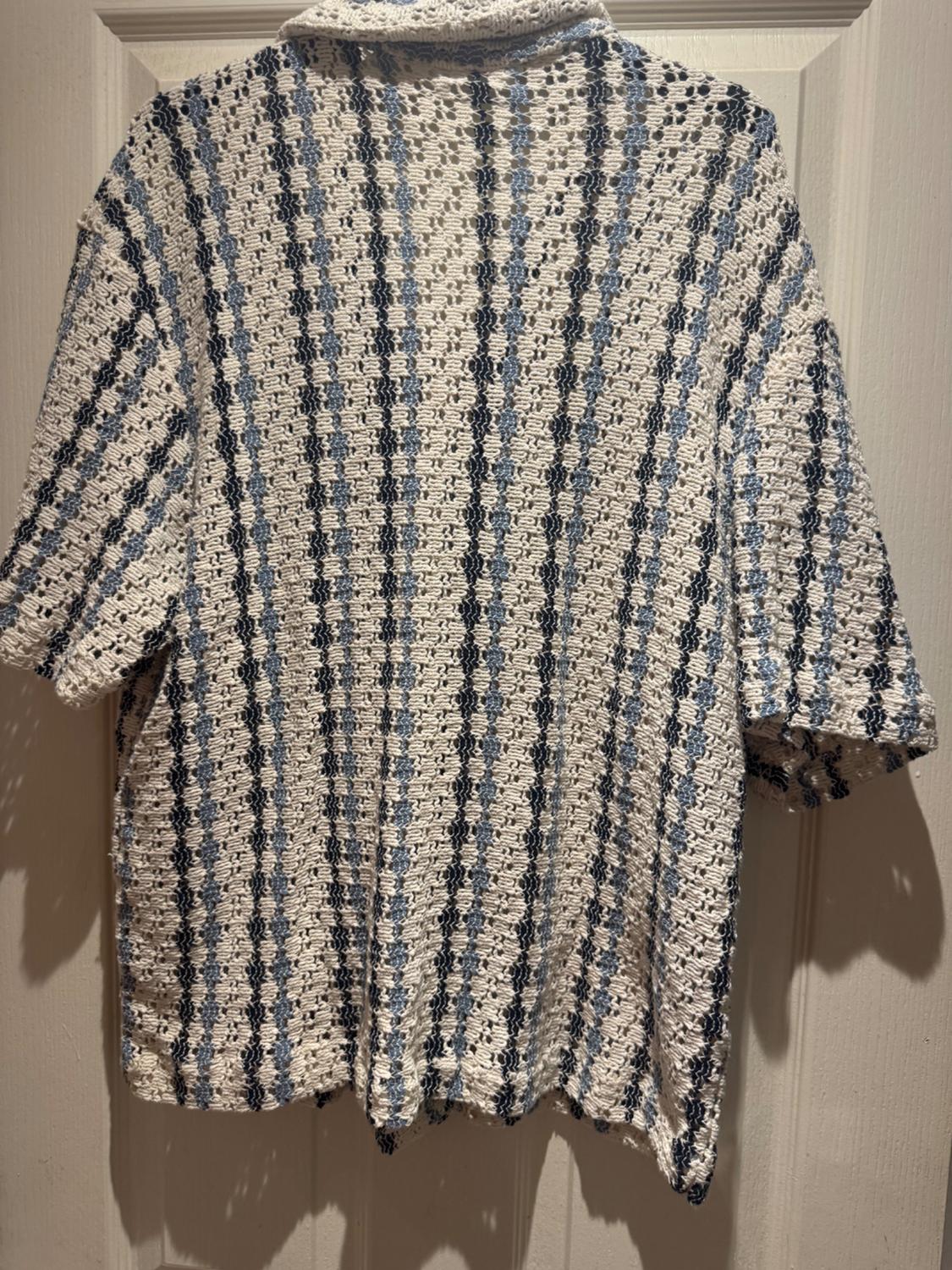 Crochet shirt with vertical stripes in white and blue, hanging on a white door.