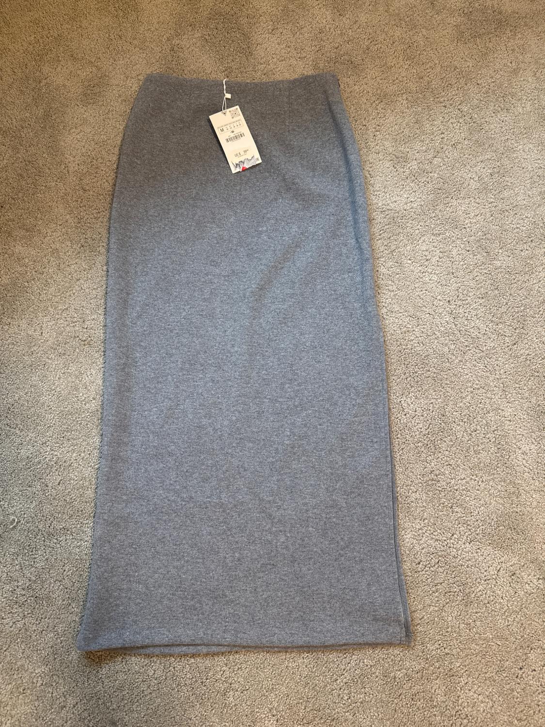 Gray long skirt on a beige rug, with a hangtag showing the price and barcode.