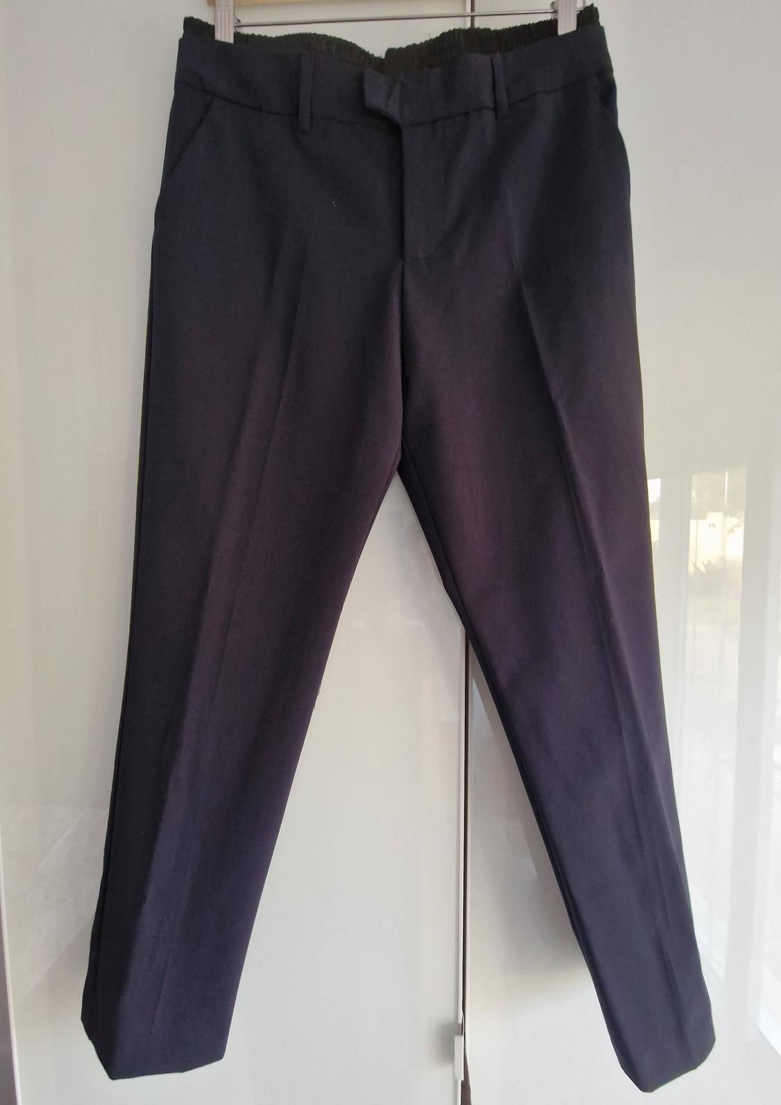 Dark formal trousers with a front crease and elasticated back waistband, hanging on a hanger in front of a white wardrobe.