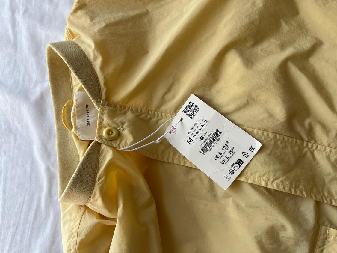Yellow garment with tag. Text: ZARA ORIGINS, SIZE M M 40 M M M, ART: 3046/315/727, US $129.00, UK £79.99.