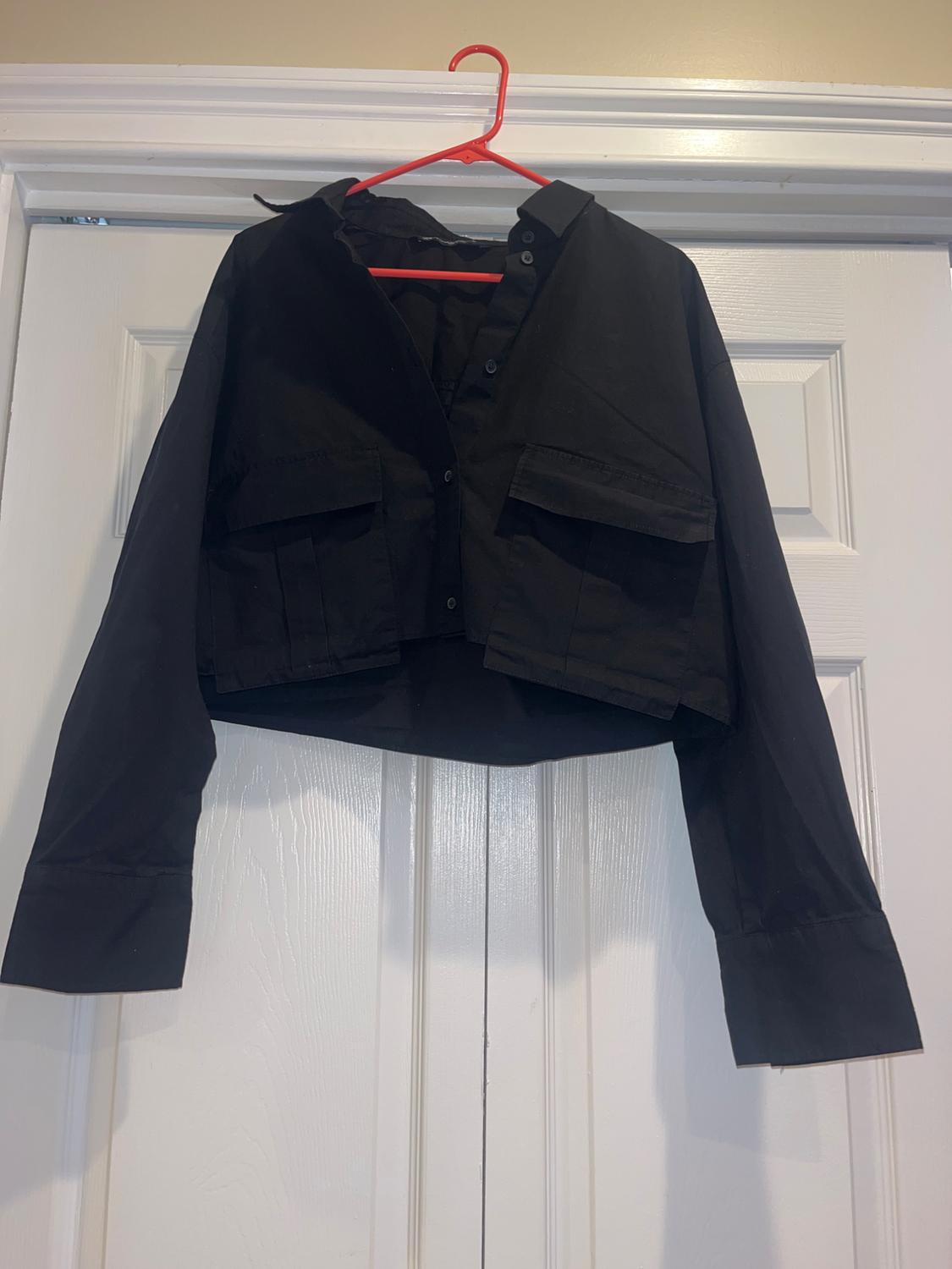 Short black jacket with front pockets, hanging on a red hanger over a white door.