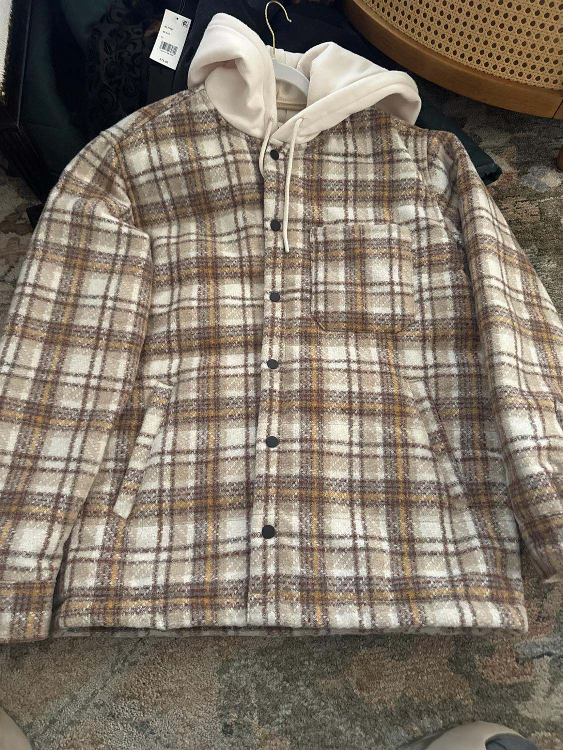 Beige and brown checked jacket with a white hood and dark buttons, laid out on a patterned rug.