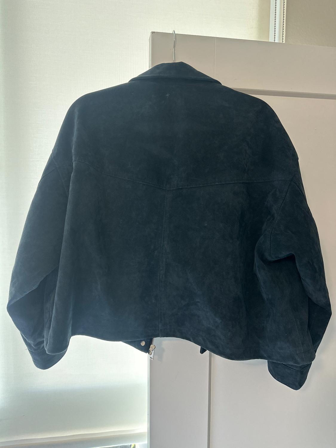Dark blue suede jacket hanging on a white door, seen from behind. Natural light illuminates the background.
