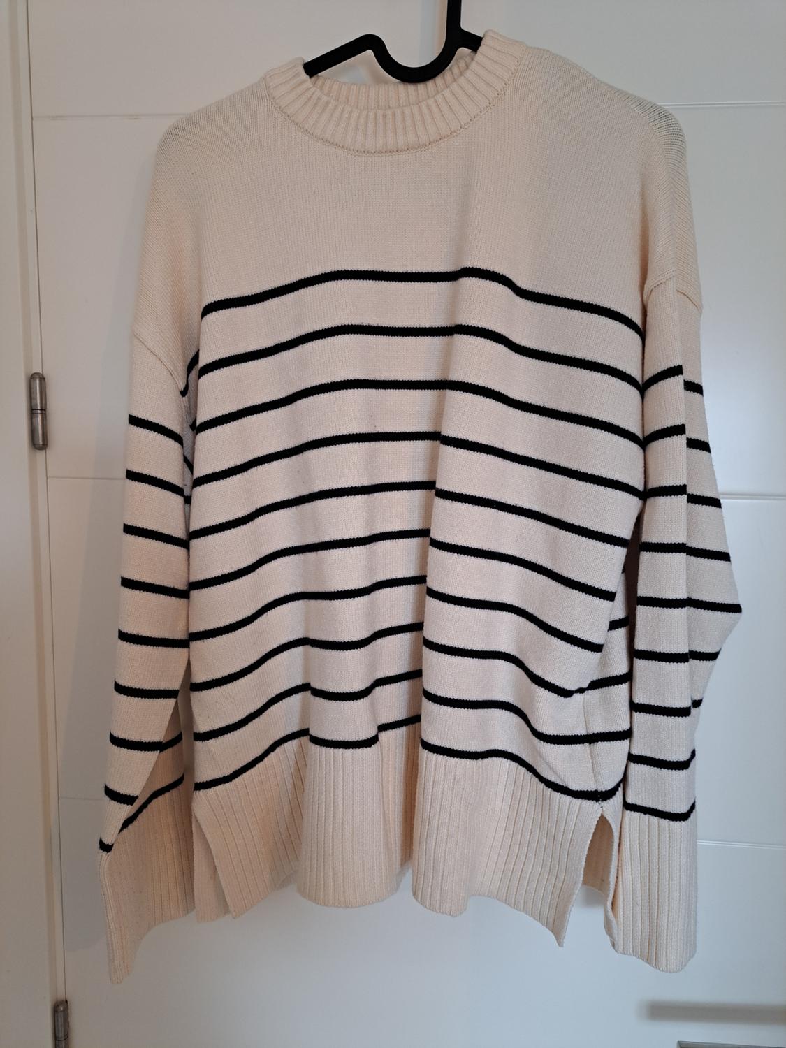 Beige knitted jumper with black horizontal stripes, hanging on a black hanger over a white door.