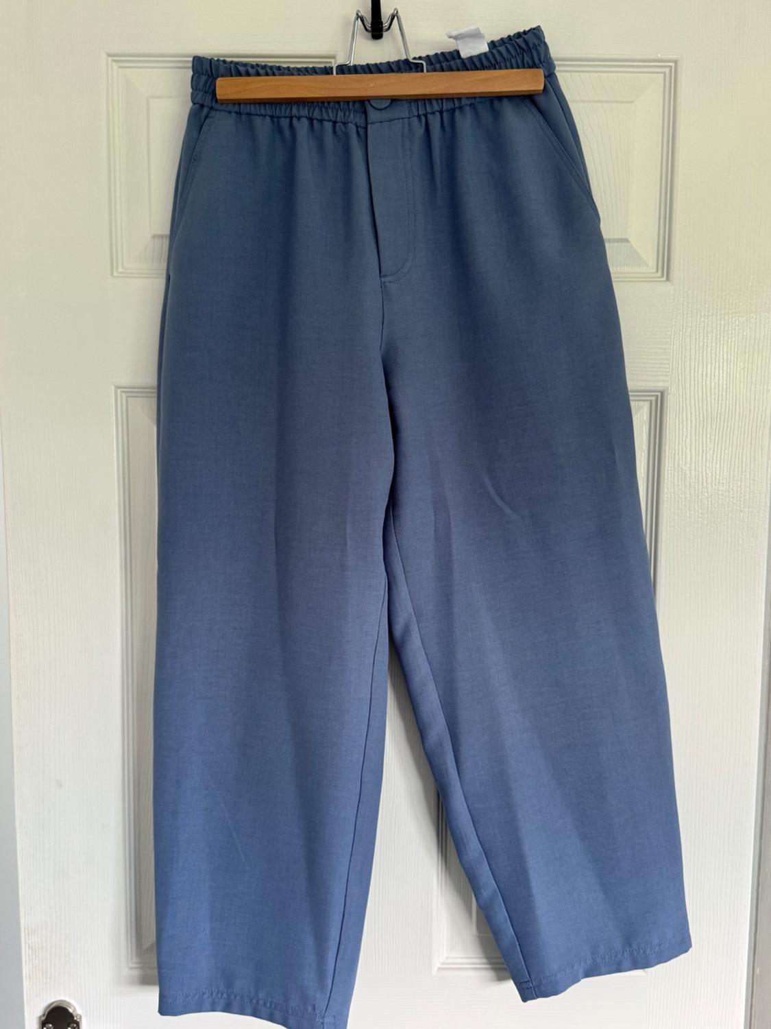 Blue trousers hanging on a wooden hanger over a white door. Elasticated waist design and straight leg.