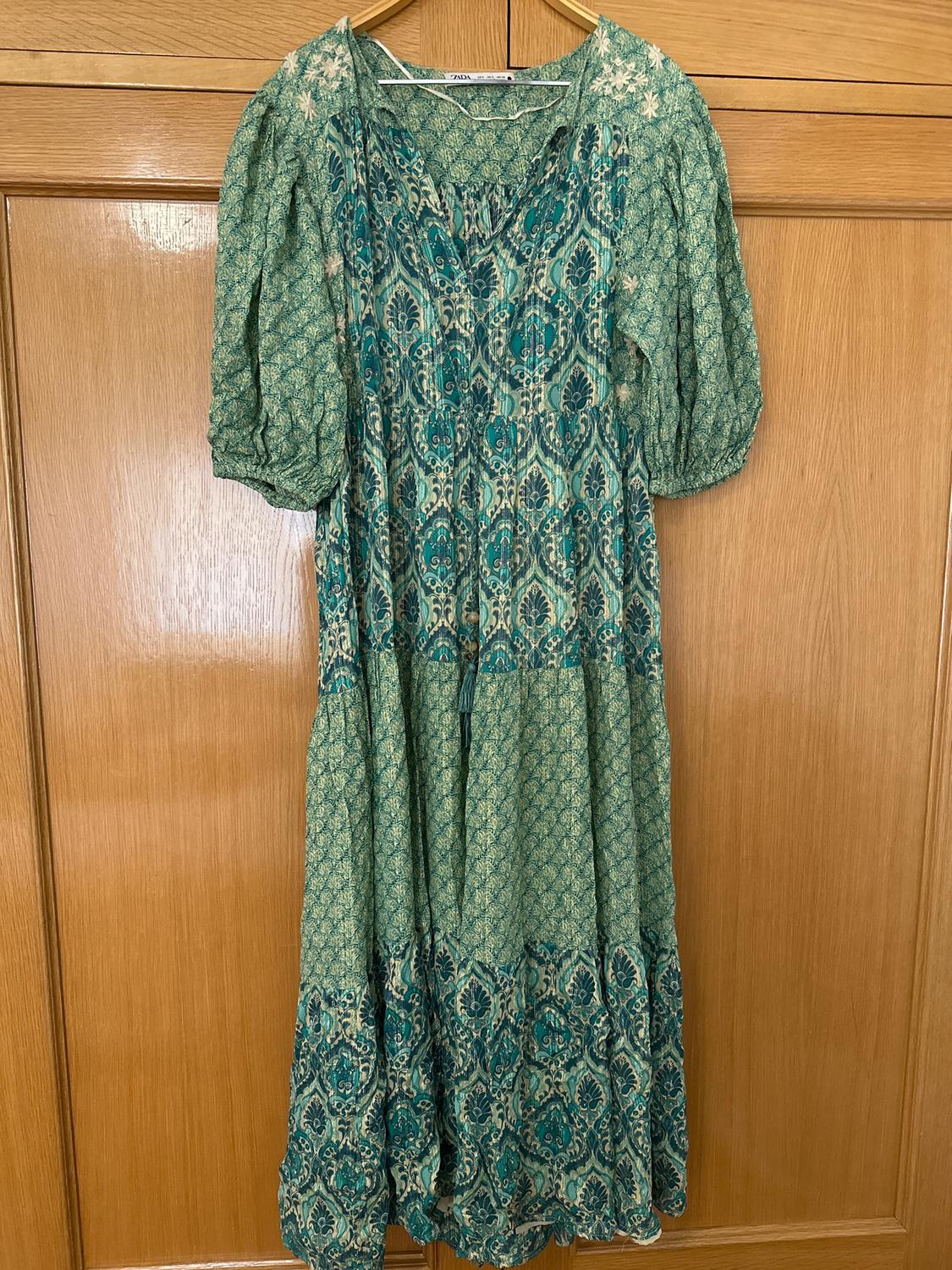 Green floral print dress hanging on a wooden door. Puffed short sleeves and V-neckline.
