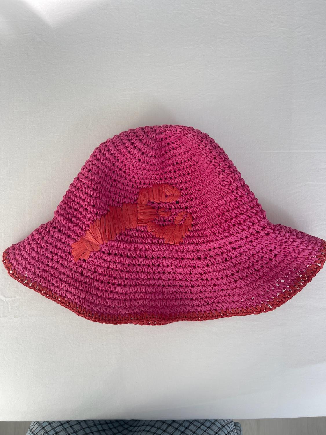 Pink woven bucket hat with a red lobster in the centre and red trim, on a white surface.
