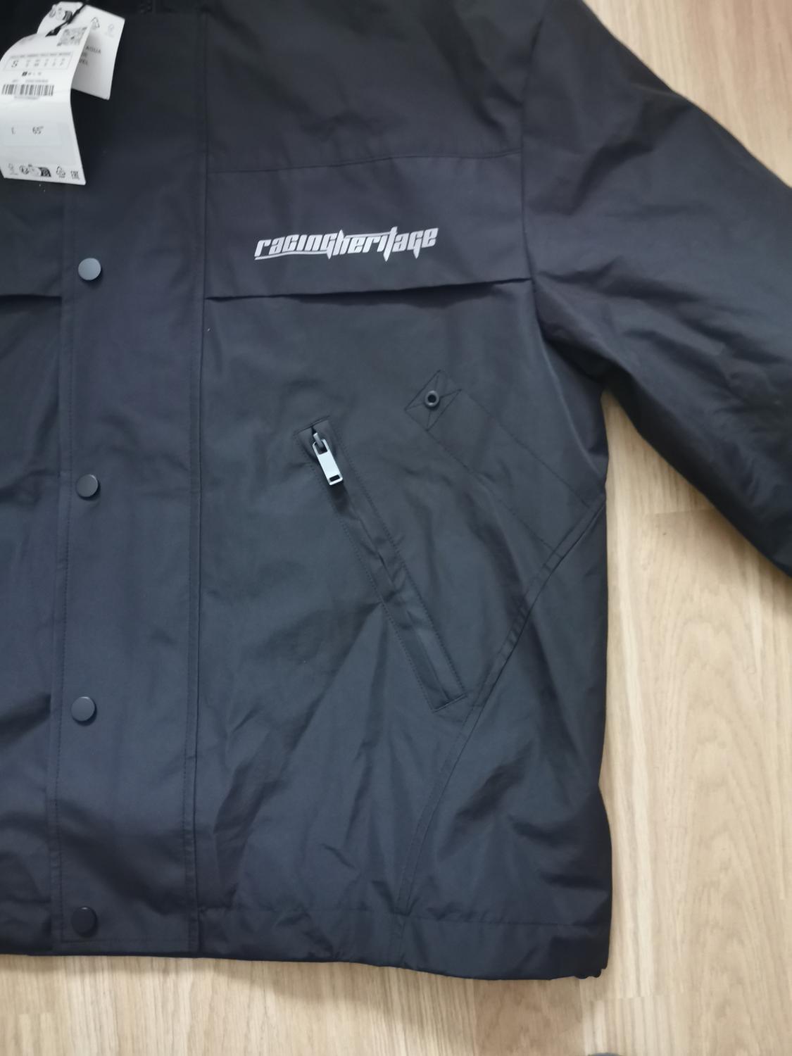Black jacket with button fastening and zip pocket. "racingheritage" inscription on the chest. Visible labels.