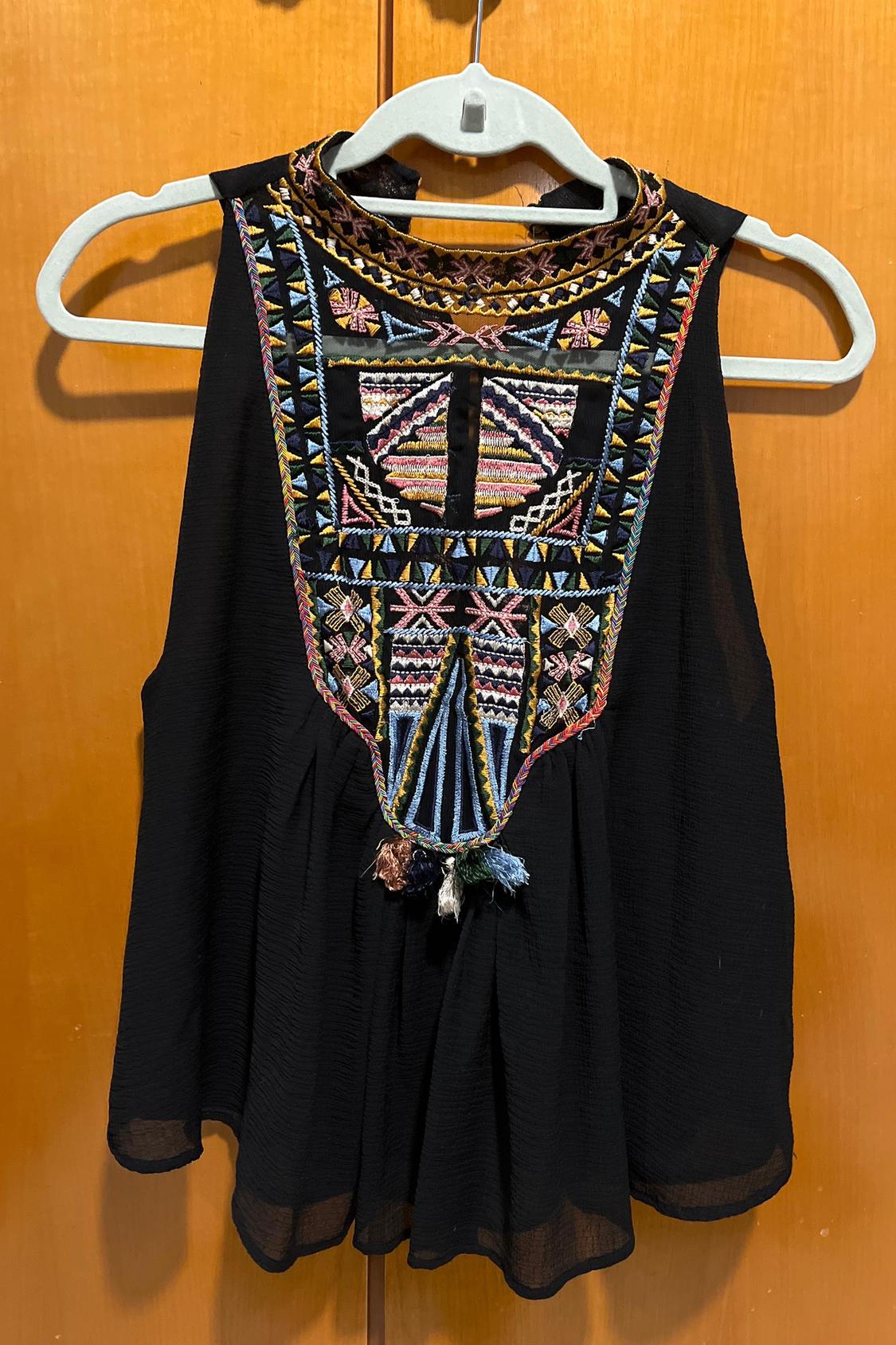 Front view of black blouse with colourful geometric embroidery on the chest and round neck.